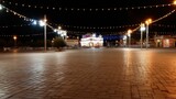 Beautifully illuminated carnival entrance gate stands at night, adorned with festive lights, creating vibrant atmosphere. empty plaza showcases cobblestone pavement, enhancing enchanting scene