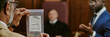© AnnaStills - Middle aged Caucasian man holding evidence bag with gold jewelry in courtroom while Black man in suit gesturing during legal proceedings, judge sitting in background