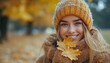 © Verla - Woman smiles holding autumn leaves in a knitted hat