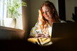 © Westend61 - Woman with red hair working remotely in a cafe with laptop and phone