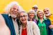 © Westend61 - Cheerful senior man taking selfie with friends in front of wall