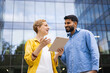 © sofiko14 - Two colleagues discuss something on a tablet in front of a modern building.
