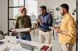 © TrueFrame Collective - Medium long shot of three Indian men working in modern office discussing business project