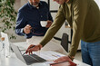 © TrueFrame Collective - Selective focus shot of two male managers looking at laptop screen working on business plan in modern office