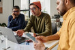 © TrueFrame Collective - Selective focus shot of three South Asian men sitting at table in office looking at laptop screen and discussing project