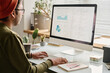 © TrueFrame Collective - Young man wearing casual clothes working with trading stats on desktop computer in modern office