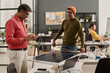 © TrueFrame Collective - Medium long shot of mature Indian man checking data on digital tablet while his younger colleague measuring size of solar panel at work in office