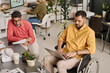 © TrueFrame Collective - High angle view of young Indian man with disability typing on laptop, his colleague sitting next to him doing paperwork