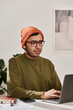 © TrueFrame Collective - Vertical medium shot of young Indian man wearing casual clothes with eyeglasses typing on laptop