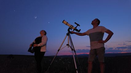Wall Mural - Amateur astronomers using telescope and binoculars for watching stars, Moon, planets and other celestial objects from a countryside field in nature.