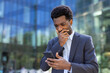© Liubomir - A businessman wearing a suit checks his smartphone outside a office building, displaying worry and focus. The image highlights urban life, technology integration, and professional challenges.