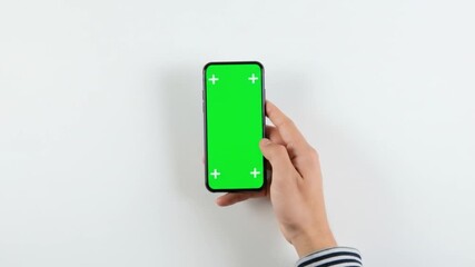 Person using a smartphone with a green screen display on a white surface, finger touching the screen