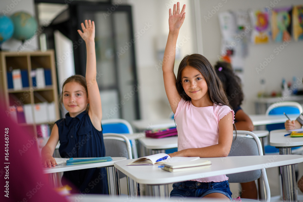 School children sitting at the desk in classroom on the lesson, raising ...