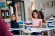 © Halfpoint - School children sitting at the desk in classroom on the lesson, raising hands.