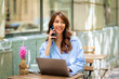 © sepy - Brunette haired woman sitting in an outdoor cafe and using smarpthone and computer laptop