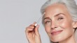 © Newleks - Senior woman with gray hair gently applying anti aging serum to forehead using pipette, highlighting skincare routine for mature complexion