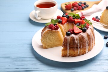 Wall Mural - pieces of delicious bundt cake with berries, glaze and mint on light blue wooden table, closeup
