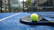 © NOOR - A lime tennis ball sits on a black paddle on a textured blue court in front of a black net