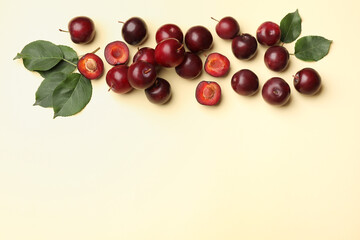 Wall Mural - whole, cut cherry plums and green leaves on light yellow background, flat lay. space for text