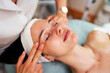 © Dusko - Professional beautician gently massaging face of female client lying on massage table with closed eyes, enjoying relaxing treatment in beauty salon