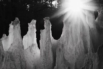 Wall Mural - Sunbeams illuminate a landscape of towering, textured rock formations, creating a dramatic black and white scene.