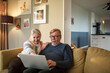 © Marko Geber - Happy senior couple using laptop together at home on the couch