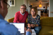 © Marko Geber - Senior couple meeting with financial advisor at home with laptop and documents