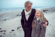 © Marko Geber - Senior couple walking on the beach in winter coats and smiling together