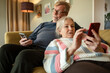 © Marko Geber - Senior couple relaxing on the couch at home using smartphones together