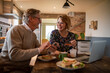 © Marko Geber - Happy senior couple shopping online together at home while having breakfast on kitchen table