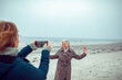 © Marko Geber - Senior woman smiling and posing for a photo on a cloudy beach taken by a friend
