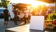 © Nabil - Blank white sign in front of a vibrant food truck scene during sunset, providing space for customization for menus, advertisements, or special event promotions.