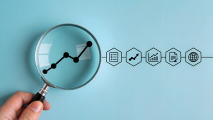 A minimalist business analytics concept showing a magnifying glass held by a hand enlarging a graph and a series of icons.