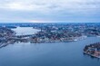 © AmazingAerialAgency - Aerial view of the shimmering water weaving through Stockholm's islands, crowned by historic buildings and the distant glow of the setting sun, Stockholm, Stockholm County, Sweden.