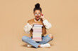 © ViDi Studio - Full length young fun surprised girl student wear casual clothes glasses backpack bag sitting hold stack of many paper books isolated on plain beige background. High school university college concept.