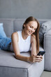 © F8  \ Suport Ukraine - Young woman sit relax on sofa in living room browsing surfing wireless internet on smartphone.