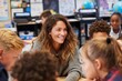 © Vovmar - Portrait of smiling primary school teacher at her desk surrounded by children. Teacher and children meeting at school after holidays.