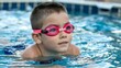 © Salauddin - Close up of a young boy wearing pink swimming goggles looking up with a determined expression while in a swimming pool