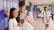 © Monkey Business - Two High School Or Secondary Students Looking At Social Media Or Internet On Phone By Lockers