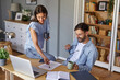 © Stockphotodirectors - A woman leans over a desk to point at notes while a man sits casually, holding a mug and smiling. Sunlight fills the home office, creating a warm and inviting atmosphere.