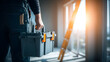 © plaksa - Close-up of a worker in dark coveralls holding a gray toolbox with orange handle, indoor setting with bright sunlight streaming through window, ladder in the background, cinematic industrial atmospher