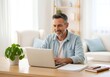 © Jay - Smiling Middle-Aged Man Working on Laptop in Bright Home Office