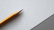 © artwiyanastudio - A sharpened yellow pencil rests diagonally on textured white paper, meeting a grey surface.  Clean lines, minimalist aesthetic