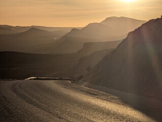 Wall Mural - winding mountain road at sunset with silhouettes of hills and a warm golden sky in morocco