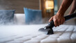 © Annamorphosis - Person's hand using a vacuum cleaner to clean a bed mattress.