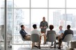 © CollyWang - A man is speaking to a group of people in a modern office with large windows.
