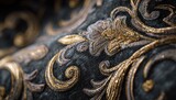 Close-up of dark fabric with gold and silver ornate floral embroidery, showing intricate detail and texture