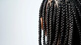 A close-up of tightly woven black braids against a plain white background. The texture is intricate and uniform, highlighting the skillful craftsmanship of the braiding technique.