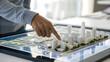 © Boontharika - Geospatial Analytics A person points at a modern city architectural model displayed on a digital touchscreen table.