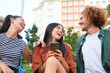 © Ladanifer - Three happy young multiracial friends are using a smartphone and laughing together in a city park
